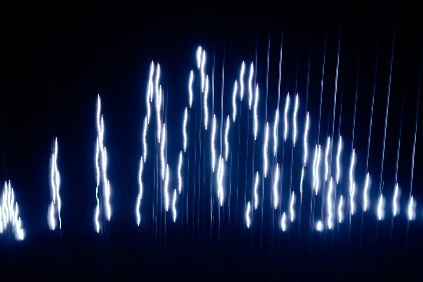 Abstrakte blaue und weiße Lichtwellen, die sich gegen einen dunklen Hintergrund erheben.