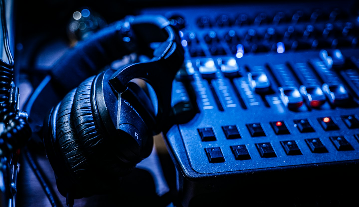 Schwarze Kopfhörer auf einem Audio-Mischpult mit blauem Licht.